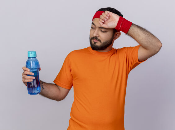 奶瓶疲惫的年轻人戴着头带和腕带 拿着水瓶 用手在白色背景上擦额头前额头带手