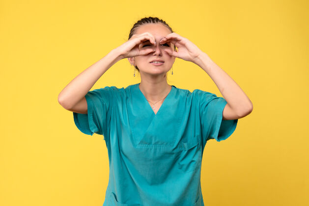 女人前视图穿着医用衬衫的女医生透过手指看 健康护士医院的covid-19病毒颜色通过手指女性