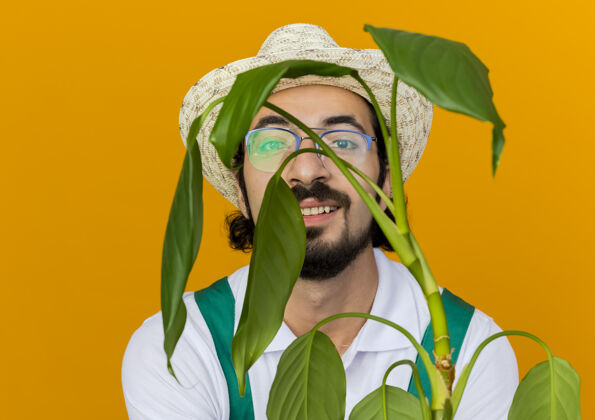 光学戴着园艺帽 戴着眼镜的快乐的男园丁抱着植物看园艺穿眼镜