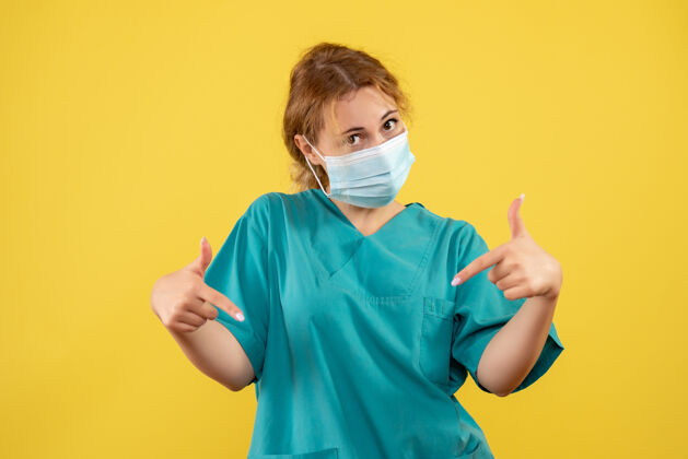 成人黄色墙壁上穿着医疗服 戴着口罩的女医生的正视图面部人面罩
