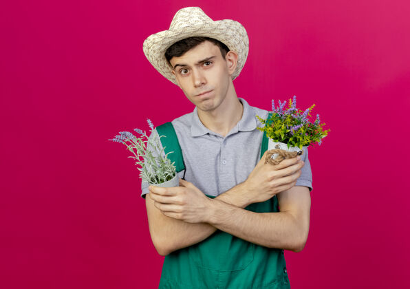 手臂自信的年轻男园丁戴着园艺帽交叉双臂捧着花盆帽子交叉粉红色