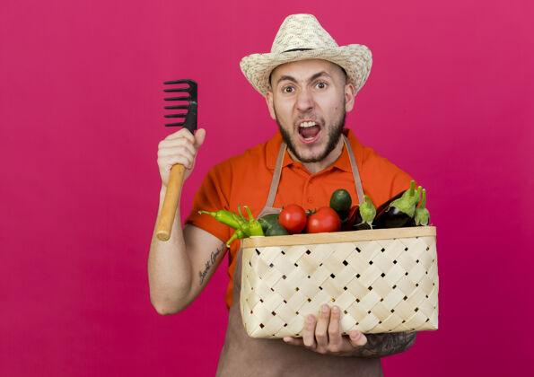 持有愤怒的男园丁戴着园艺帽 手里拿着菜篮和耙子蔬菜愤怒耙