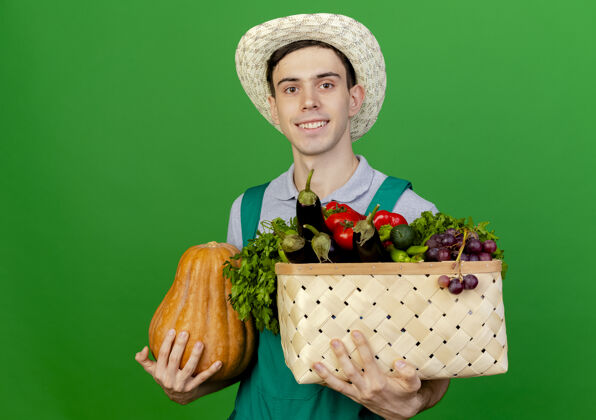 南瓜微笑的年轻男园丁戴着园艺帽 手里拿着南瓜和菜篮看着穿篮子复制