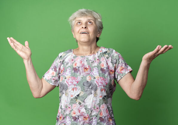 举起来惊讶的老妇人举手看着绿色的墙壁向上老的老的