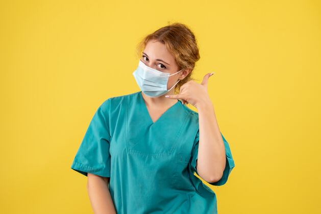 女医生黄色墙壁上穿着医疗服 戴着口罩的女医生的正视图正面肖像病毒