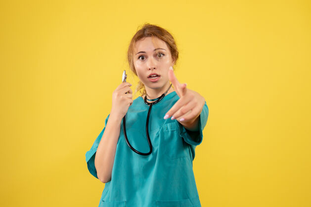 病毒黄色墙壁上穿着带听诊器的医疗服的女医生的正视图快乐套装听诊器