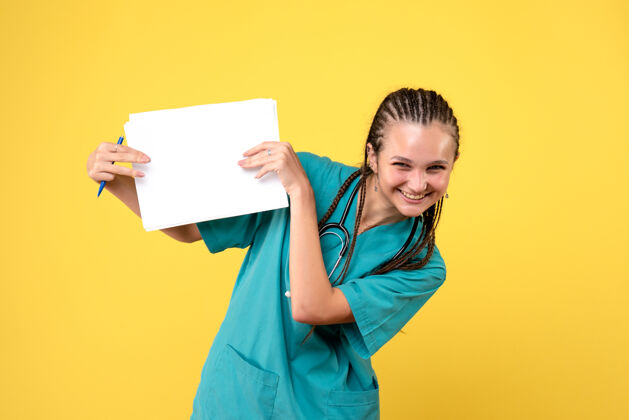 健康黄墙上穿着医疗服拿着纸的女医生的正视图医疗女医生前面