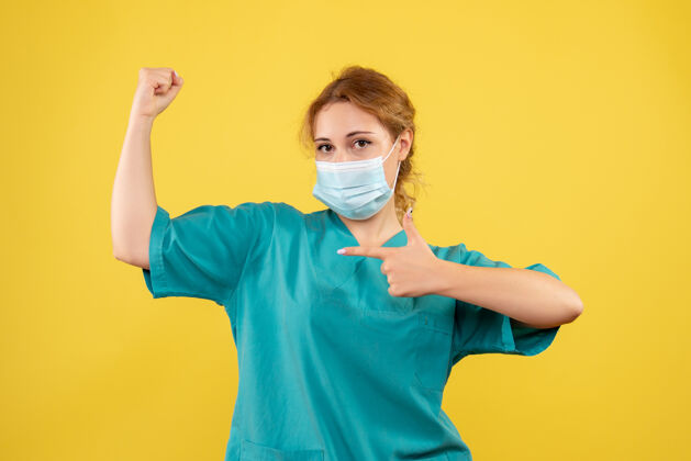 肖像黄色墙壁上穿着医疗服 戴着口罩的女医生的正视图医疗套装女医生