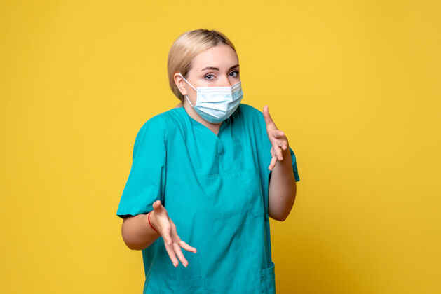 医疗黄墙上年轻女医生穿着医用衬衫 戴着口罩的正面图情绪微笑流行病