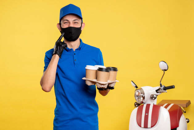 人正面图：戴着黑色口罩的男快递员拿着咖啡在黄色的工作台上递工作服工作黄色人