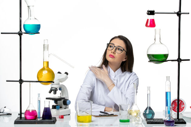 微笑前视图穿着白色医疗服的女化学家坐在白色背景的科学病毒冠状病毒-大流行实验室上拿着溶液前面解决方案科学