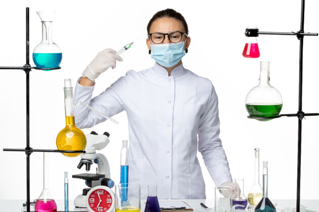 男性前视图：穿着医疗服的女化学家 戴着面罩 在浅白色背景上拿着注射液病毒化学实验室covidsplash西装持有病毒