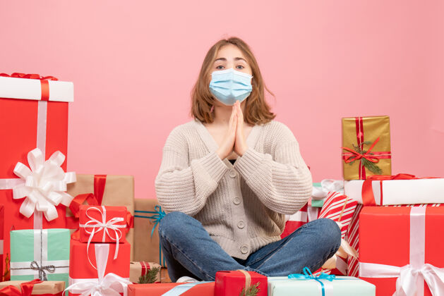 年轻女性正面图：坐在圣诞节周围的年轻女性戴着无菌面具出现病毒绝育坐着