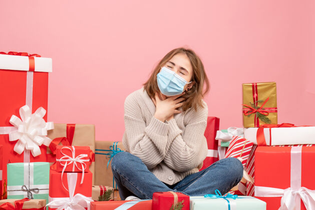 人正面图：坐在圣诞节周围的年轻女性戴着无菌面具出现消毒颜色休闲