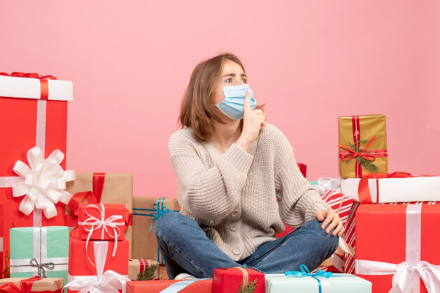 成人正面图：坐在圣诞节周围的年轻女性戴着无菌面具出现人情感礼物