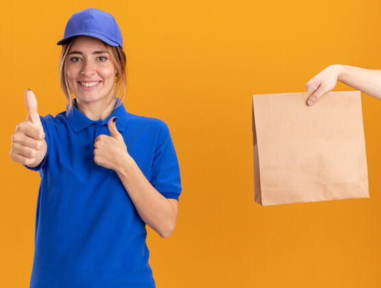 年轻有人把纸包给了身着制服 面带微笑的年轻漂亮的女送货员 她竖起大拇指 两只手放在橘子上交货制服手