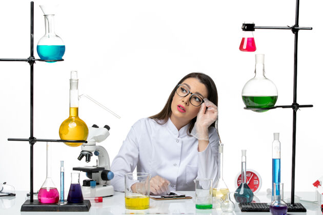 大流行前视图穿着白色医疗服的女化学家坐在那里 拿着解决方案在白色背景上写笔记科学大流行病毒covid实验室实验室实验室前面