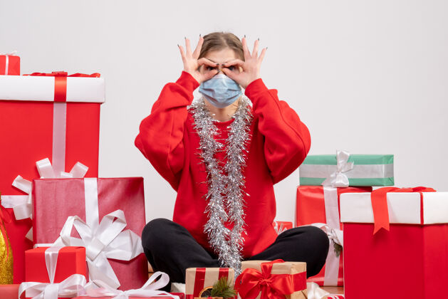 礼物正面图：年轻女性戴着无菌面具坐着 手里拿着圣诞礼物服装面具坐着