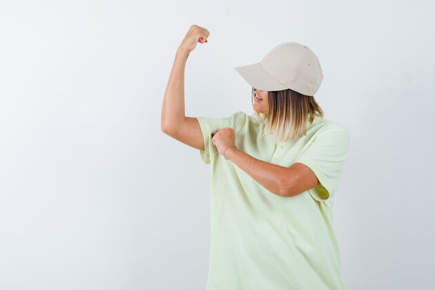 自豪年轻女性穿着t恤 戴着帽子 露出手臂的肌肉 看上去很自豪 前视图皮肤头发魅力