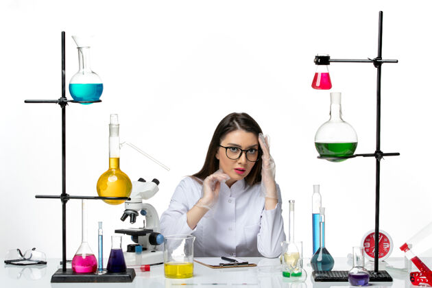 烧杯前视图穿着白色医疗服的女化学家坐在浅白背景上实验室病毒冠状病毒大流行科学液体视图病毒