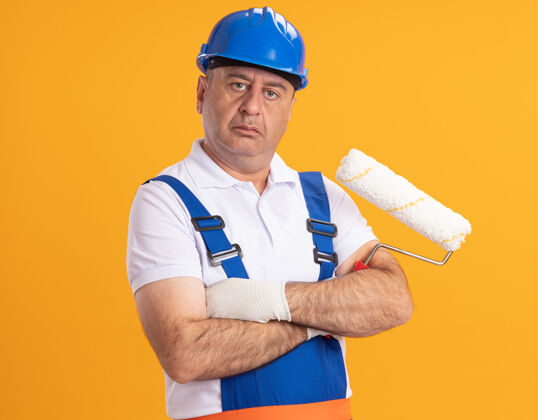 人自信的白人成年建筑工人身着制服 双臂交叉 手持橙色的滚轴刷立场信心人