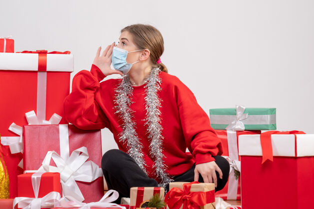 面具正面图：年轻女性戴着无菌面具坐着 手里拿着圣诞礼物年份病毒漂亮