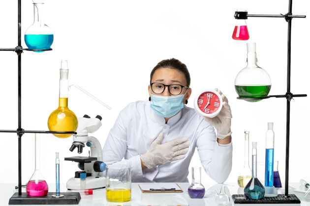 飞溅前视图身穿医疗服的女化学家 戴着面具 白色背景上拿着红色的时钟病毒化学冠状病毒-飞溅实验室外套西装化学
