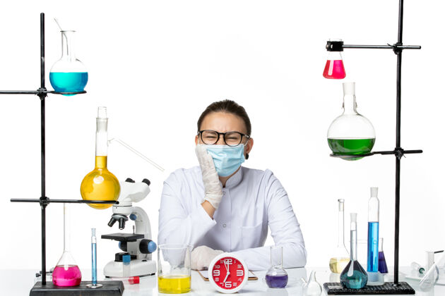 医疗前视图穿着医疗服的女化学家戴着口罩坐着 白色背景上有牙痛的溶液化学病毒实验室病毒-飞溅前面解决方案化学