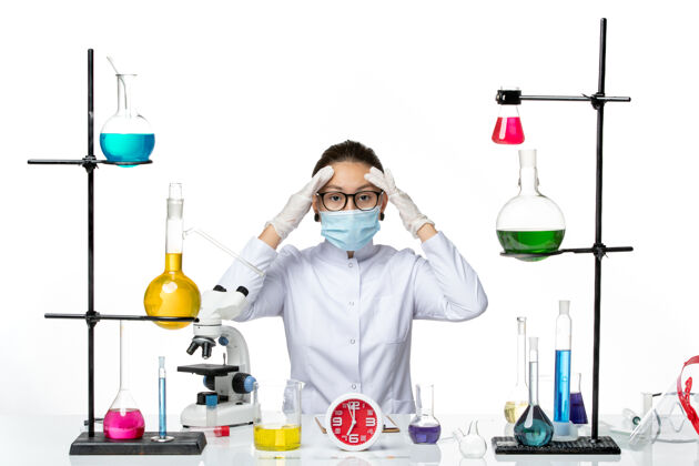 视图前视图穿着医疗服的女化学家带着面罩坐在浅白色背景上的溶液化学家实验室病毒-飞溅化学家人面具