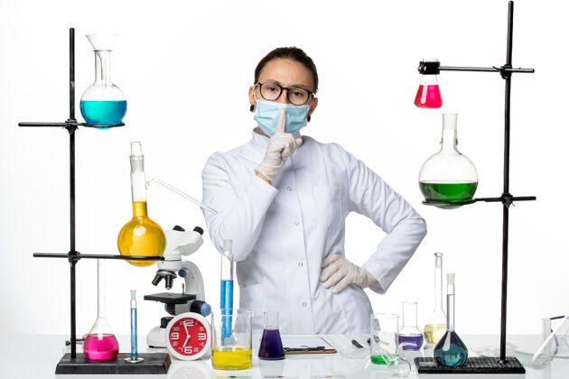 医药前视图身穿医疗服的女化学家戴着口罩站在浅白色背景上病毒化学实验室covid-splash专业前面病毒