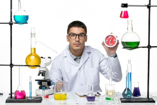 病毒正面图身穿白色医疗服的男性化学家拿着白色背景上的时钟-冠状病毒疾病科学实验室时钟套装实验室