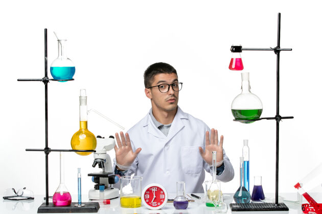 科学正面图身着白色医疗服的男性化学家坐在浅白背景上 用不同的溶液研究病毒科学实验室的病毒大流行前面罐子实验室
