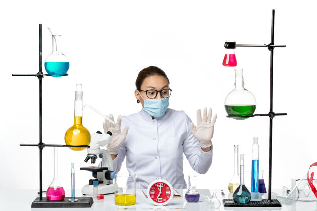 坐着前视图穿着白色医疗服的女化学家戴着口罩坐在白色地板上拿着解决方案化学家病毒冠状病毒-飞溅实验室医学实验室喷溅