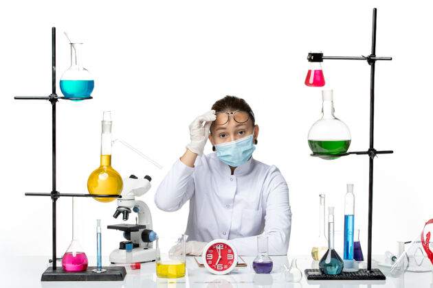 前面前视图穿着医疗服的女化学家带着面罩坐在白色背景上 溅起病毒化学covid实验室的溶液医生视图专业