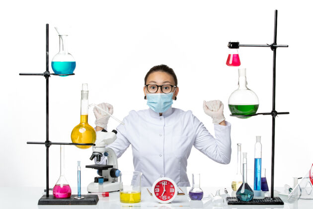 医学前视图穿着白色医疗服的女化学家带着面罩坐在白色背景上的溶液化学家病毒病毒-飞溅实验室坐着医生实验室