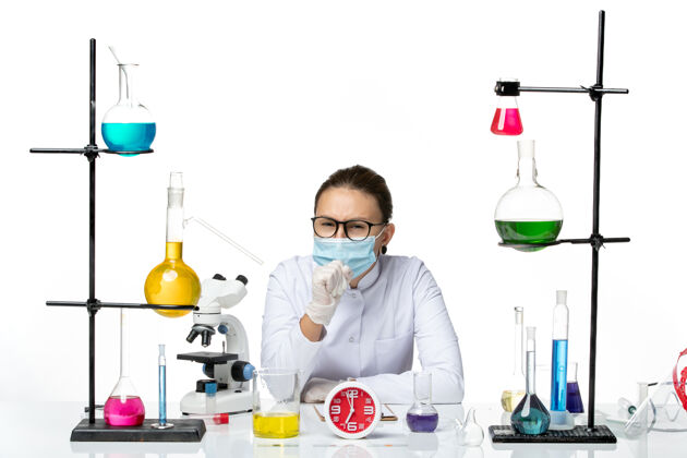 医疗前视图穿着医疗服的女化学家戴着面罩 坐在白色背景上的溶液化学病毒实验室病毒-飞溅专业视图实验室