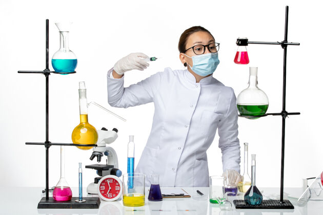 病毒前视图：身穿医疗服的女化学家 戴着面罩 在浅白色背景上注射病毒化学实验室的covid-splash视图持有实验室