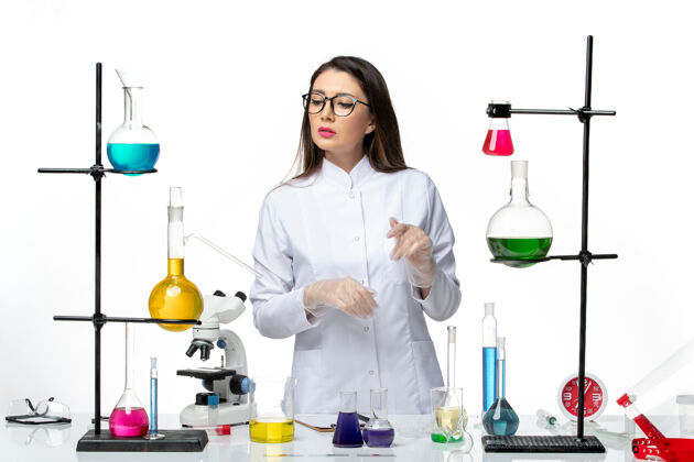 实验室正面图：身着无菌医疗服的女化学家站在桌子旁 拿着白色办公桌上的解决方案病毒疾病冠状病毒-实验室大流行科学罐子溶液周围