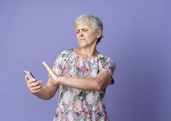 女人不高兴的老妇人拿着电话假装把电话推到紫色的墙上推紫色不高兴