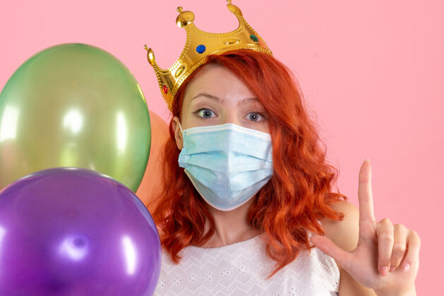 举行正面图：年轻女性手持彩色气球 戴着粉色的无菌面具消毒肖像聚会