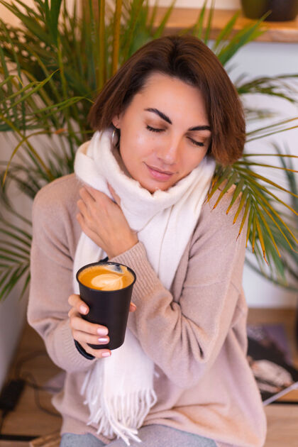 卡布奇诺一个女孩在舒适的咖啡馆里用一杯热咖啡取暖热脸羊毛
