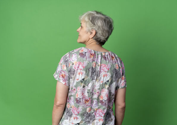 背的自信的老妇人站在一旁看 背影 孤零零的绿墙上自信老的女人