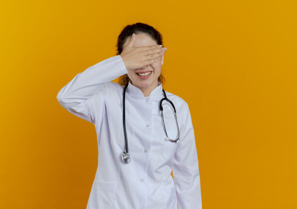 橙色面带微笑的年轻女医生 穿着医用长袍 戴着听诊器 戴着眼镜 手眼被隔离眼镜女性戴