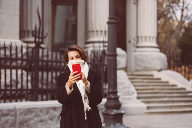 外套街上穿着黑色冬衣 戴着白色围巾 手持手机的女人的户外写真秋季探索电话