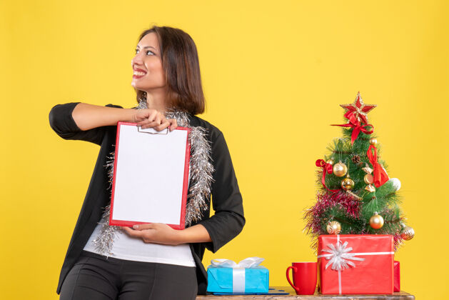 人圣诞节的心情 情绪化的美丽女士站在办公室里 拿着文件看着黄色的办公室里的东西圣诞节微笑生活