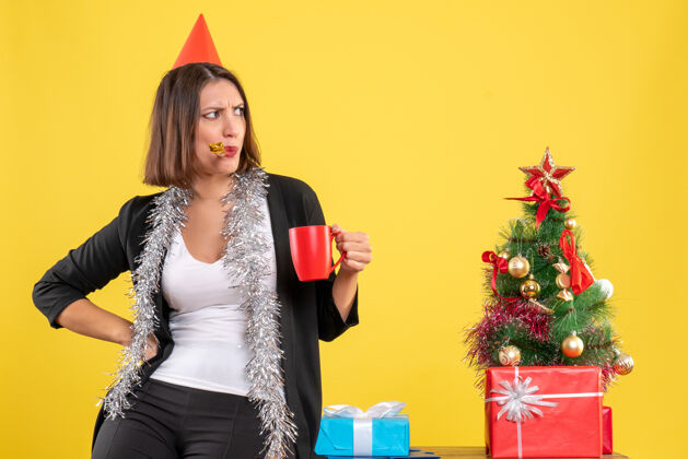 漂亮圣诞心情与迷茫美丽的女士捧着红杯子在办公室里放黄肖像性感模特