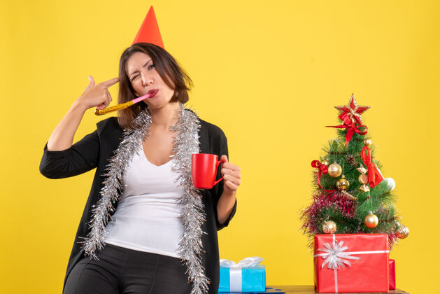 性感圣诞心情与搞笑美丽的女士手持红色杯子在黄色的办公室快乐成人性感
