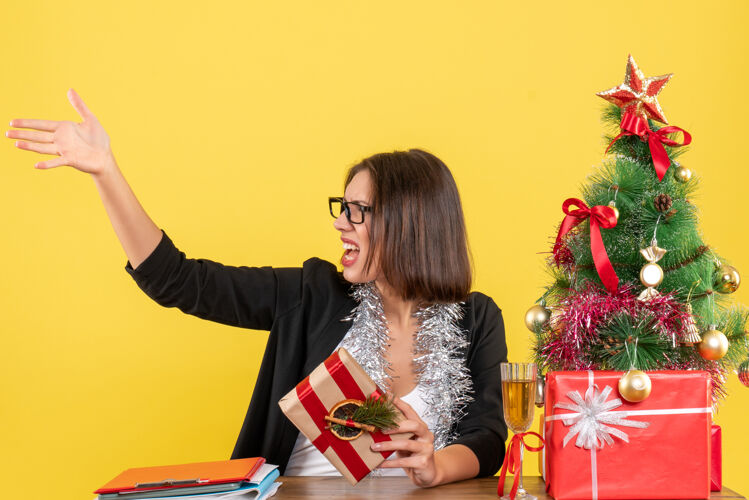 打电话穿着西装 戴着眼镜 拿着礼物的漂亮商务女士 在办公室里给坐在桌子旁 树上放着圣诞树的人打电话礼物漂亮成人
