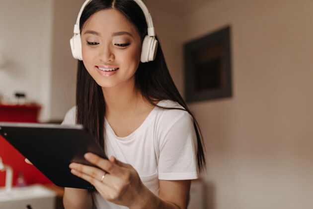 设备穿着白色t恤的晒黑女人戴着耳机听歌 看着平板电脑的屏幕沙发歌曲内部