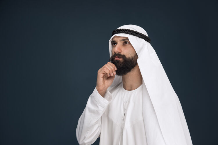 深蓝色工作室背景上的半身阿拉伯沙特商人肖像年轻的男模站着 看起来很体贴商业 金融 面部表情 人类情感的概念震惊搞笑面部